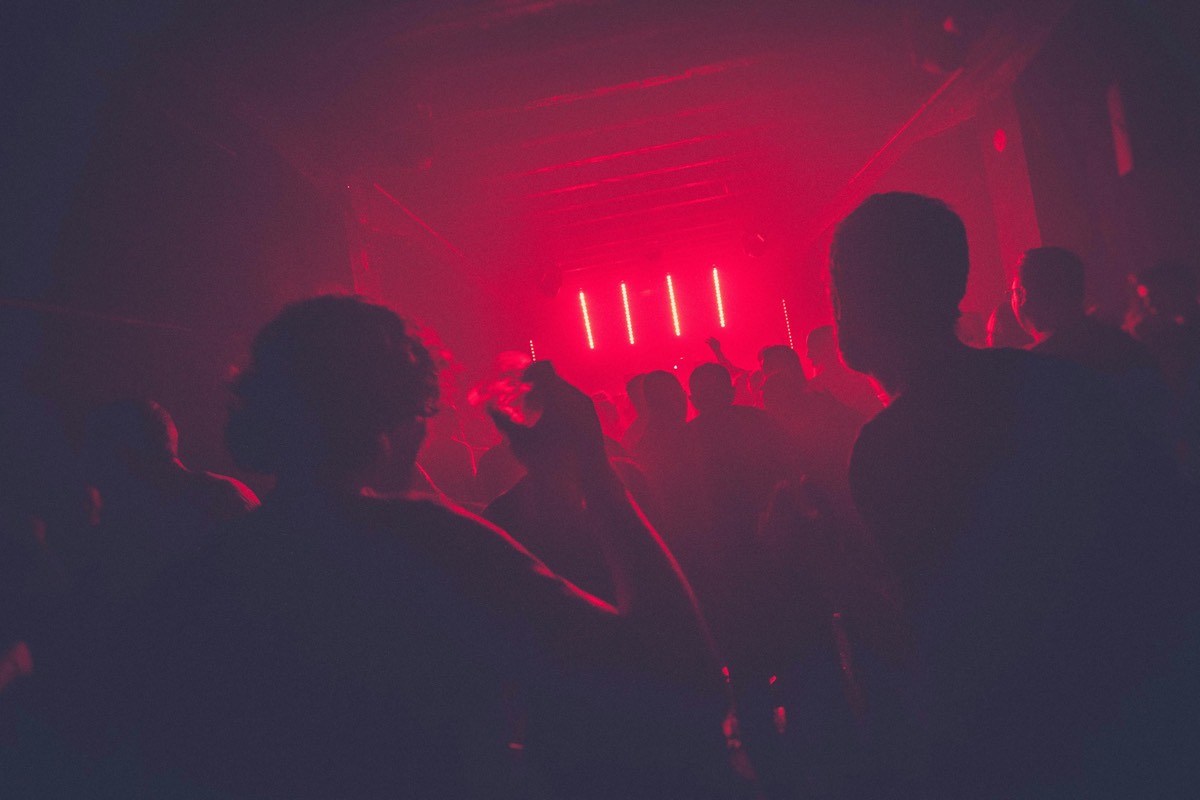 A concert crowd with hands raised under magenta light.